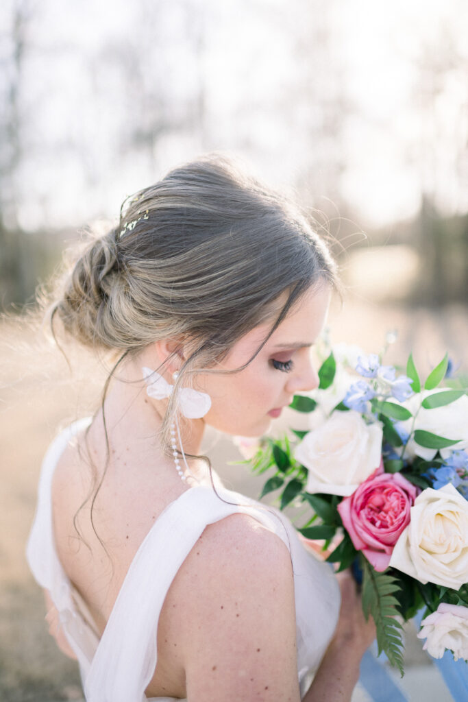 Beautiful bride looks down over her shoulder while holding colorful bouquet, flecks of gold in her hair done by Kaitlyn with Beauty on the Block.